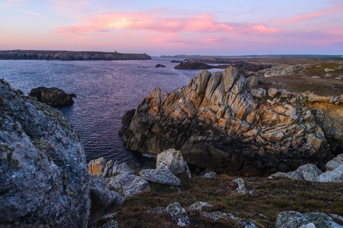 Un voile rose métallique se dépose sur la mer et les falaises.