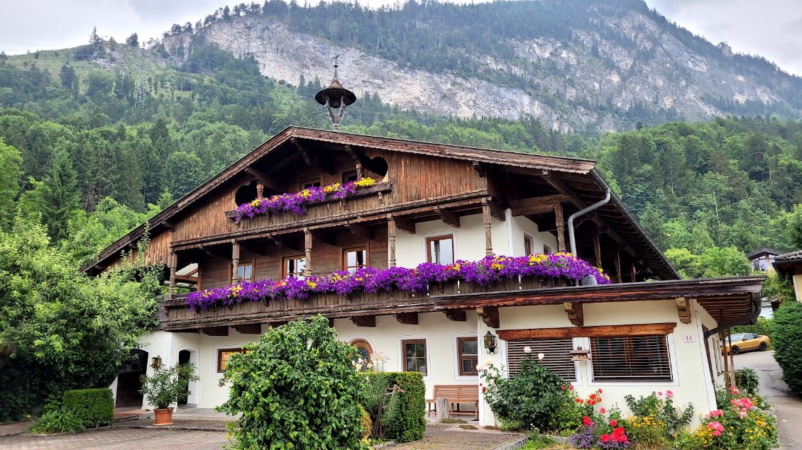 Chalet autrichien typique avec cloche sur le toit et jardinières qui débordent de fleurs.