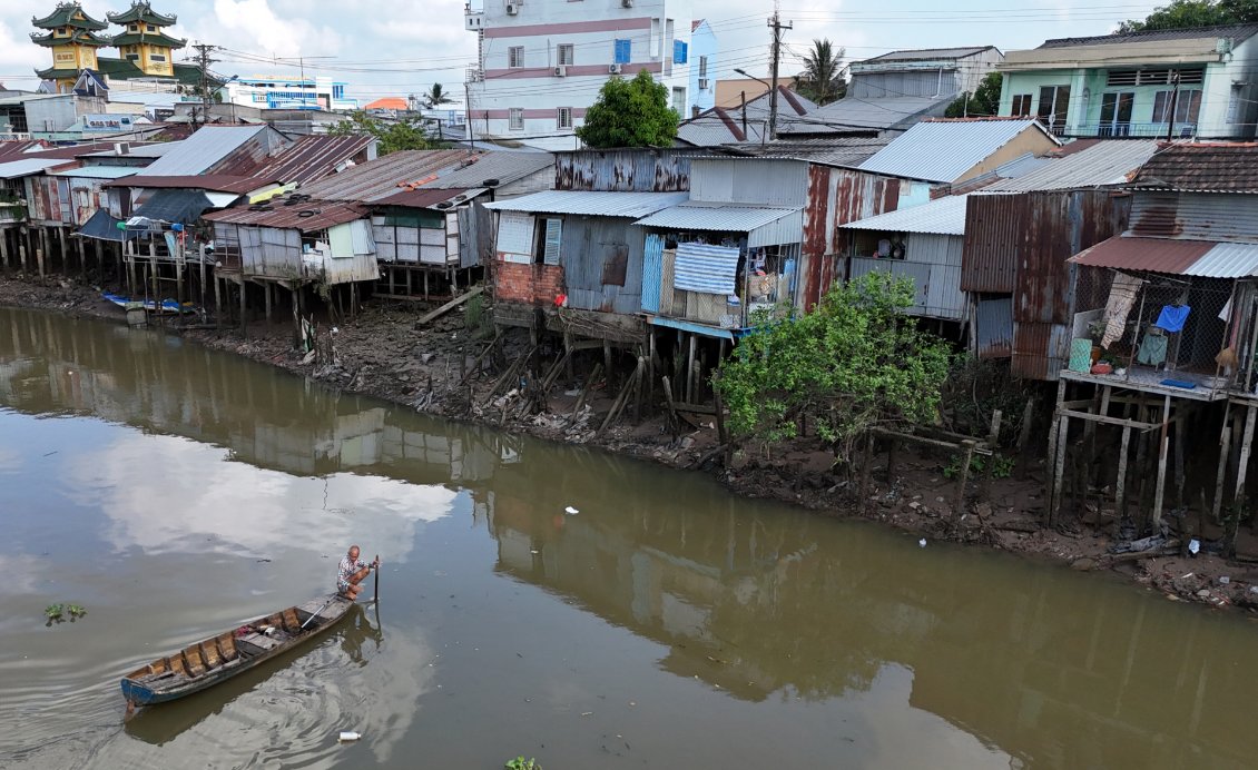 J10. A la sortie de Sa Đéc aucun mètre carré n'est perdu avec ces maisons bâties sur pilotis. L'homme dans la barque ramasse les déchets flottants.