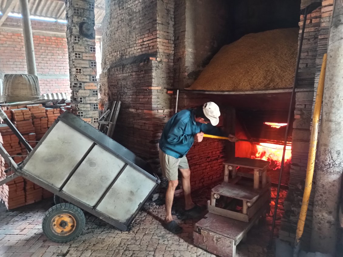 J11. L'homme aide les écorces de riz à tomber par gravité dans le fourneau. Quand il y en a trop de consumées, il les évacue avec la charette.