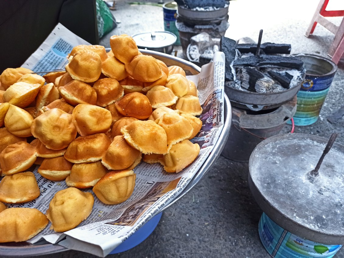 J12. Ici des gâteaux aux ingrédients plus traditionnels pour l'Europe. Ils sont cuits dans les petits moules chauffés au charbon, en arrière plan et posés à même la route.