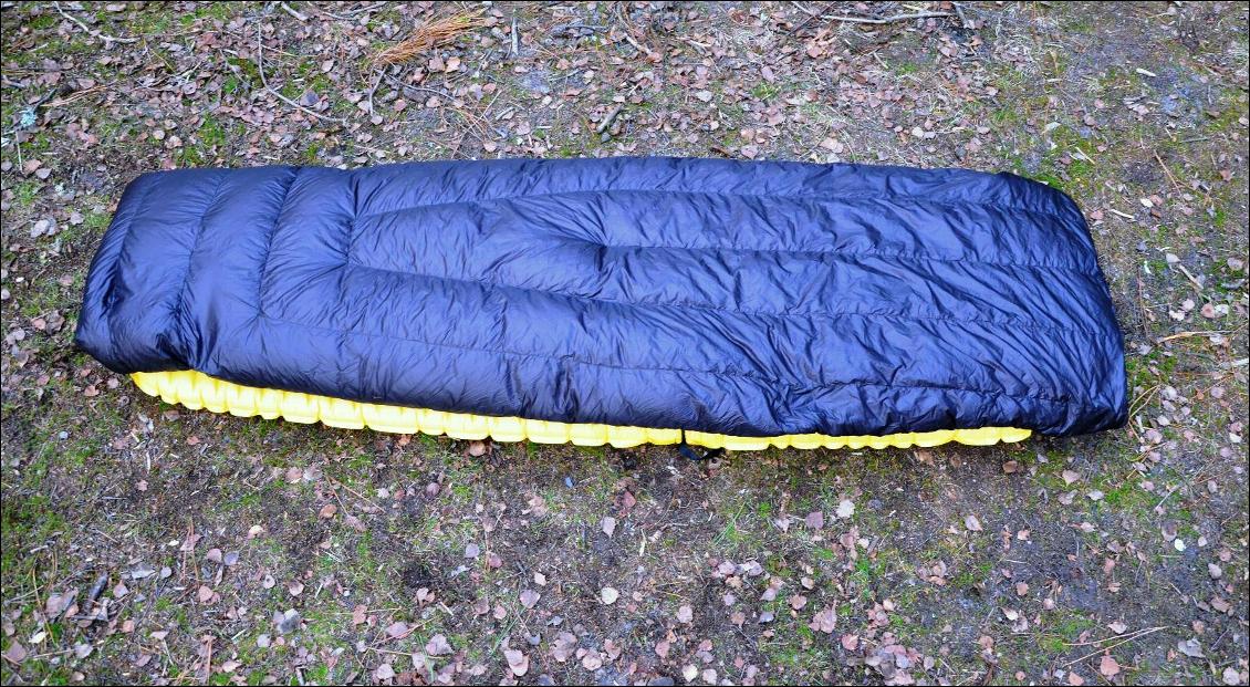 Quilt utilisé en position "couette bordée" : on voit bien les compartiments de duvet longitudinaux et sous le quilt, l'une des sangles qui permet de le fixer autour du matelas