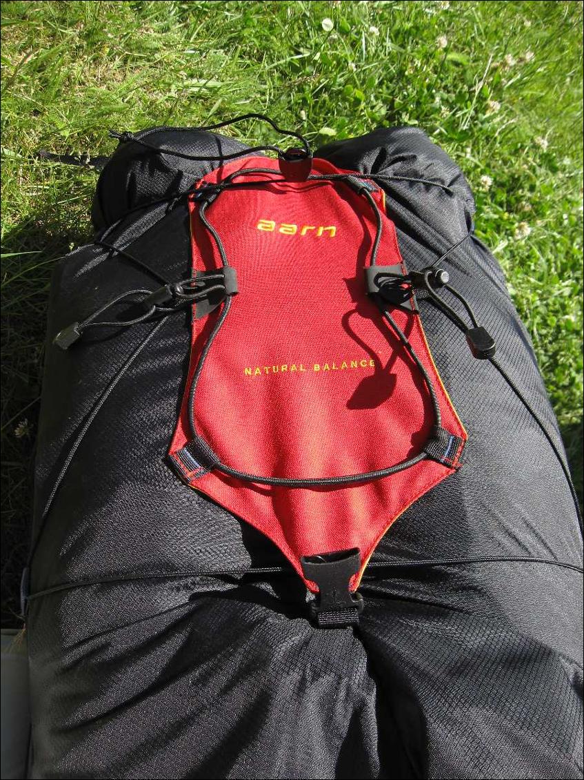 Côté avant du sac avec des porte-matériel et le cordon élastique situé sur la poche rouge ouverte (poche à crampon par exemple)